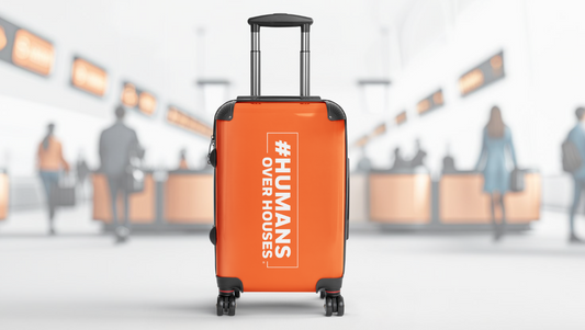 Orange suitcase with '#Humans Over Houses' text in an airport setting